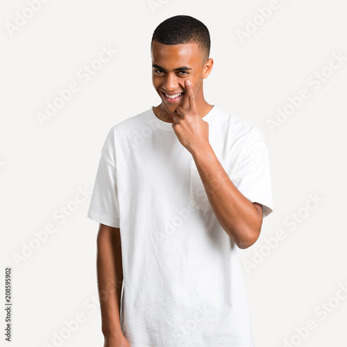 Young african american man standing and looking to the front opening the eye with finger on isolated background