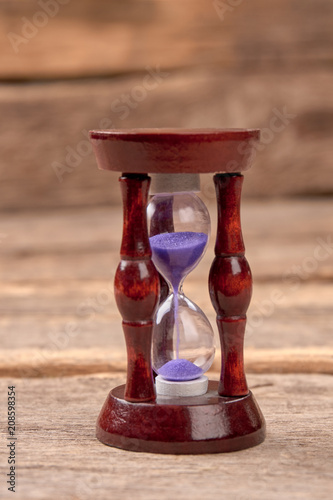 Hourglass with purple sand. Crystal hourglass on brown wood background.