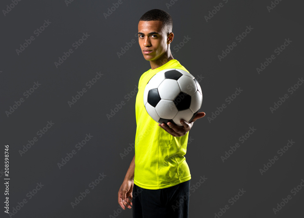 Fototapeta premium Soccer player man with dark skinned playing catching a ball with his hands on dark background
