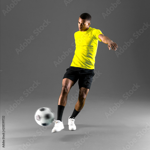 Soccer player man with dark skinned playing kicking the ball on dark background © luismolinero
