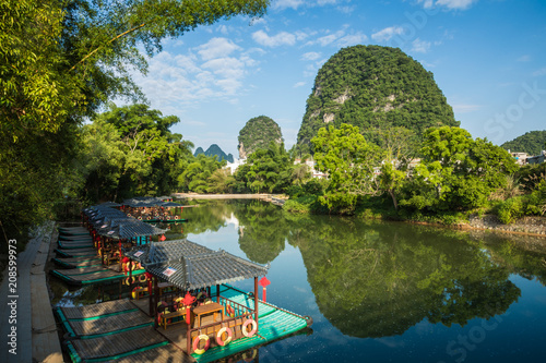 Leinwand Poster Scenic view of small tourist bamboo rafts sailing along the Yulong River among green woods and karst mountains at Yangshuo County of Guilin, China