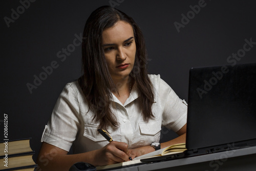 A girl uses a laptop and writes something to a notebook