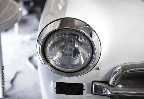 The headlight of the old car. This car is under repair. White car metal and chrome