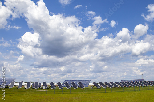Power plant solar panels on a green field under a blue sky with fluffy clouds