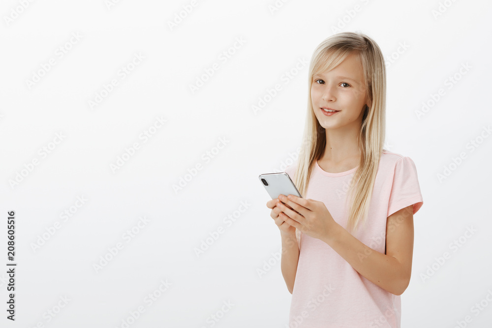 Girl can use gadgets better than parents. Portrait of confident adorable young child with pretty eyes in pink t-shirt, holding smartphone and smiling at camera, learning language with app in device Girl can use gadgets better than parents. Portrait of confident adorable young child with pretty eyes in pink t-shirt, holding smartphone and smiling at camera, learning language with app in device