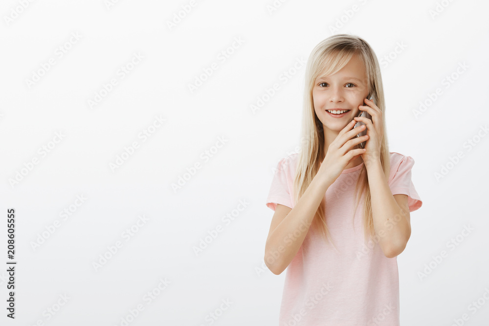 Girl staying in touch with grandparents who live far away. Portrait of pleased adorable young child in pink t-shirt, talking on smartphone and holding device with both hands, smiling broadly Girl staying in touch with grandparents who live far away. Portrait of pleased adorable young child in pink t-shirt, talking on smartphone and holding device with both hands, smiling broadly