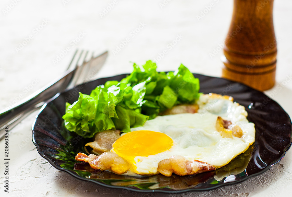 fried eggs with bacon and salad in black plate on white table fried eggs with bacon and salad in black plate on white table