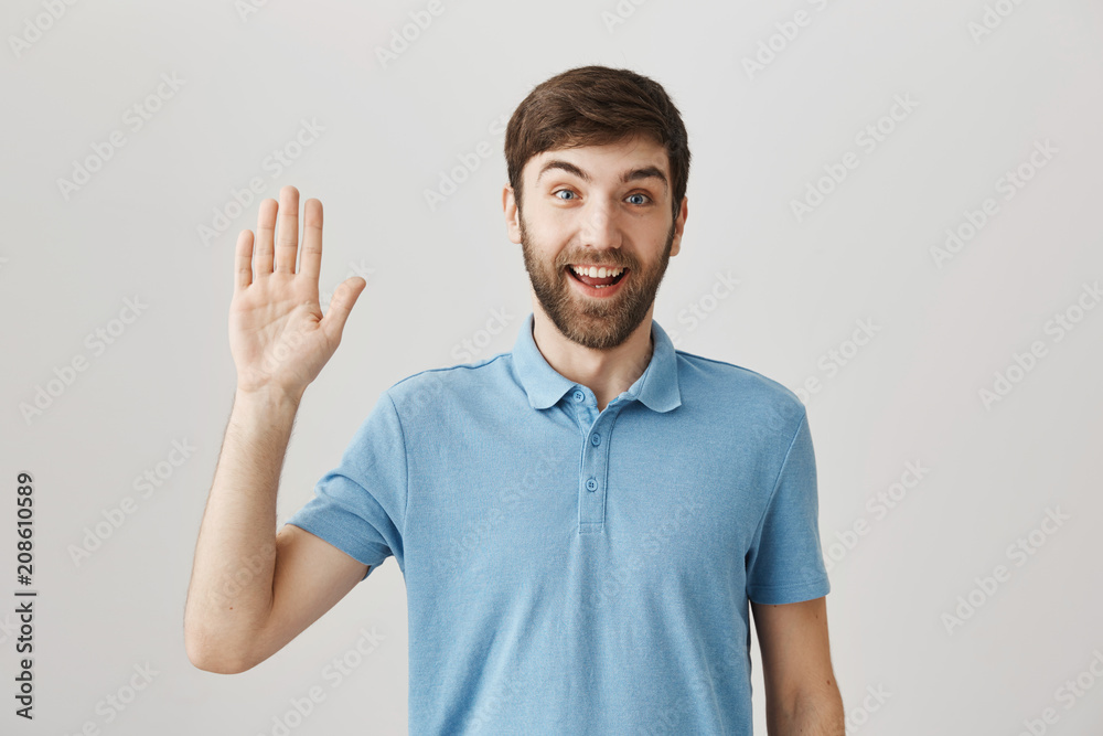 Positive bearded guy smiling friendly and waving as if greeting someone on street, expressing positive attitude and standing over gray background. Funny guy tries to establish relations with coworkers Positive bearded guy smiling friendly and waving as if greeting someone on street, expressing positive attitude and standing over gray background. Funny guy tries to establish relations with coworkers