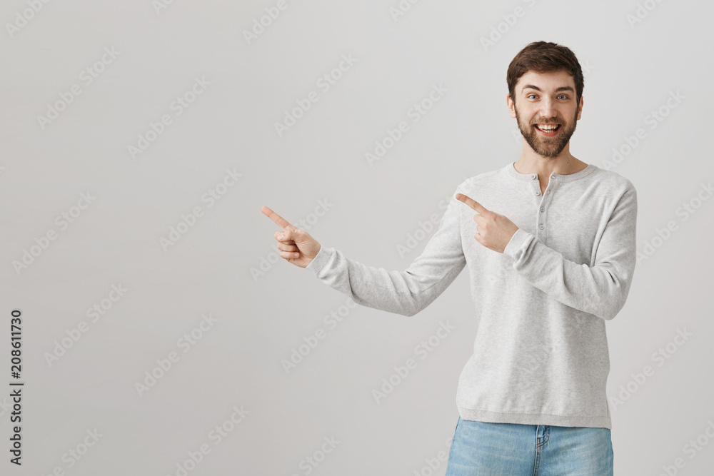 Happy good-looking caucasian bearded guy pointing left with both index fingers, smiling and being excited while standing over gray background. Upbeat boyfriend asks permission to ride roller coaster Happy good-looking caucasian bearded guy pointing left with both index fingers, smiling and being excited while standing over gray background. Upbeat boyfriend asks permission to ride roller coaster