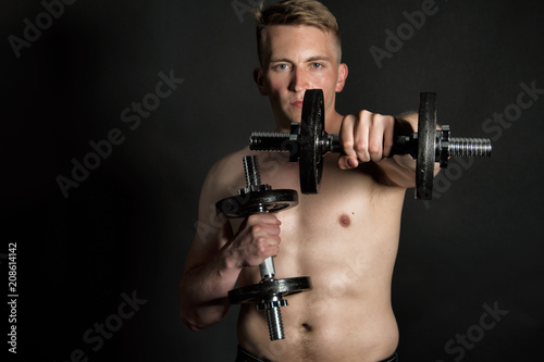 Gym and dumbbells. Young attractive guy. Black background. 