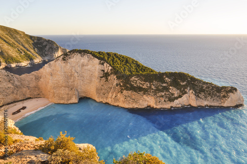 Sunset landscape from above on the most famous, vacation summer beach and bay in the world - Navagio on Zakynthos Island in Greece. Top view from rock cliff on blue sea and beach with old shipwreck.