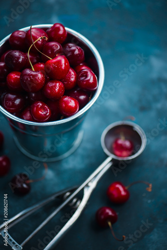 Cherries with an ice cream spoon and metal bucket on a grey concrete background, Summer berries concept with copy space. Neutral color tones still life