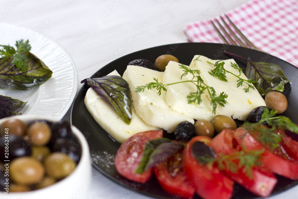 White cheese with tomatoes, green and black olives, basil, coriander and olive oil on a black plate White cheese with tomatoes, green and black olives, basil, coriander and olive oil on a black plate