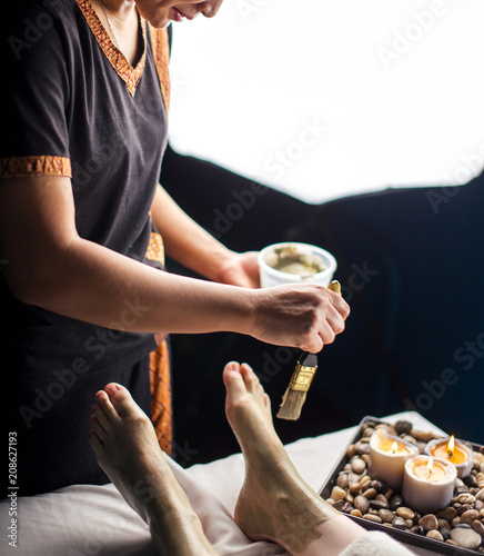 Cosmetologist doing spa treatment in salon. Girl client having clay body mask apply on foot by beautician.