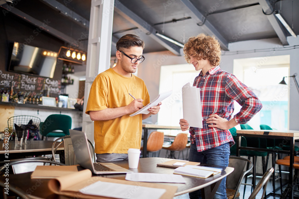Two guys in casualwear brainstorming and writing down new working ideas at meeting Two guys in casualwear brainstorming and writing down new working ideas at meeting