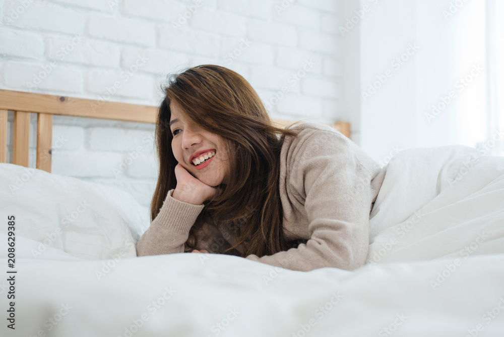 Portrait beautiful young Asian woman on bed at home in the morning. Cheerful Asian woman wearing a comfortable sweater and smiling on her bed. Relaxing room. lifestyle asia woman at home concept. Portrait beautiful young Asian woman on bed at home in the morning. Cheerful Asian woman wearing a comfortable sweater and smiling on her bed. Relaxing room. lifestyle asia woman at home concept.