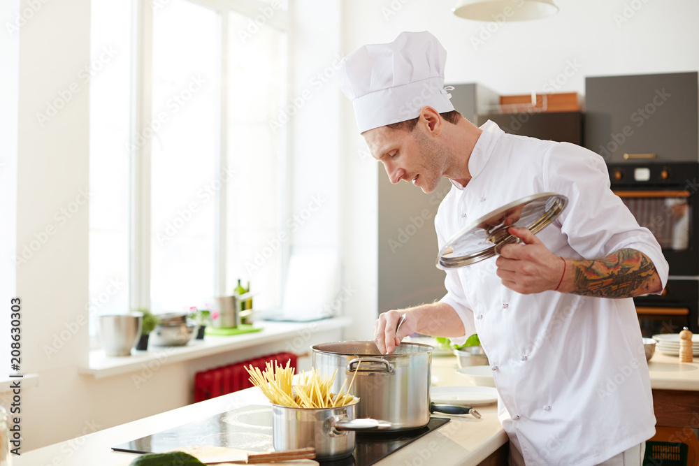 Contemporary chef mixing food in pan while cooking spaghetti on neighboring burner