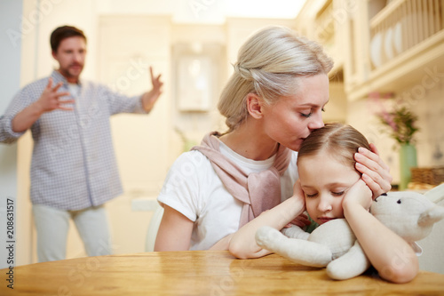 Young woman comforting little daughter while her husband shouting near by