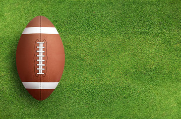 American football ball on grass field background. Football ball 3D illustration.