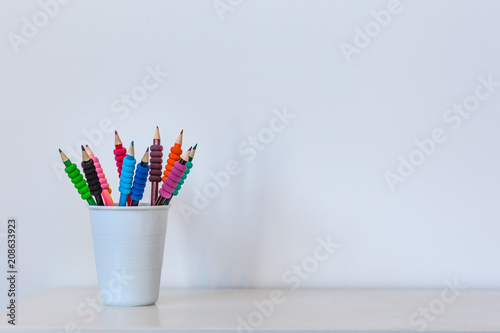 Back to school concept - colored pencils in white cup on table against white wall with copy space