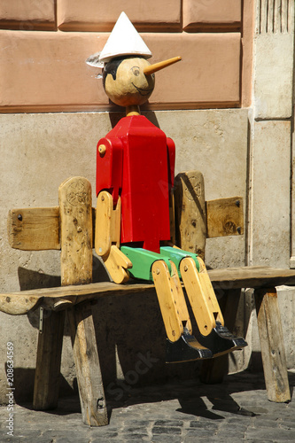 Old Pinocchio wooden marionette rom the book written by Carlo Collodi sits on a bench, Italy