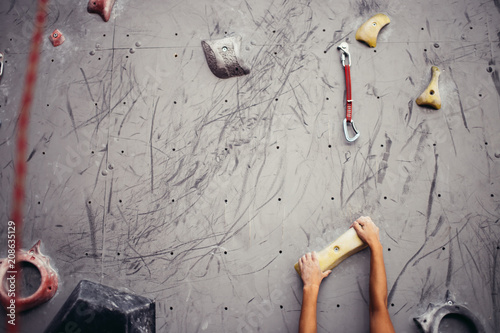 Climber hands holding artificial boulder on grey wall in climbing gym, closeup shot