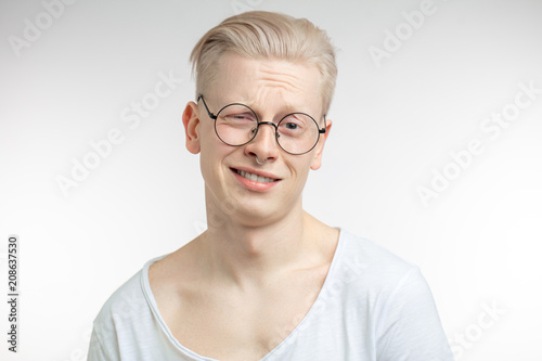 Blonde skeptical young man, in spaectacles with derisive, sneering, scornful, mocking face expression, showing no interest in conversation, isolated on white background. Emotion, facial expression