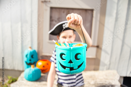 boy in a pirate costume holds a bucket with inedible gifts.  Teal Pumpkin Project. Alternative non-food treats for kids with food allergies. the concept of health for children in the Halloween season. photo