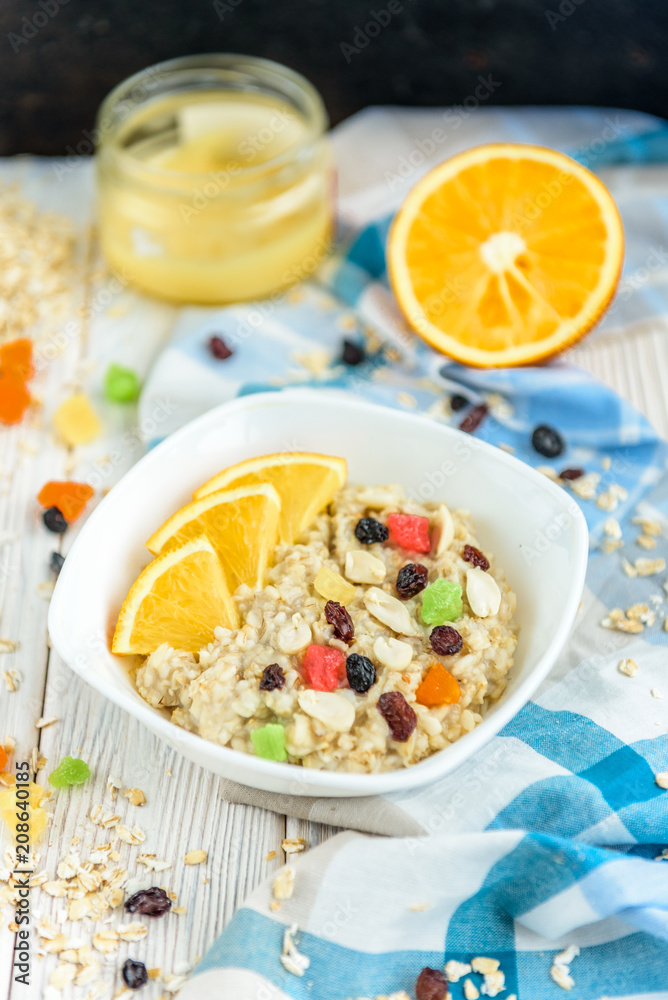 Homemade oatmeal porridge with honey, orange, raisin, peanut and candied fruit on white wooden background. Healthy breakfast. Homemade oatmeal porridge with honey, orange, raisin, peanut and candied fruit on white wooden background. Healthy breakfast.