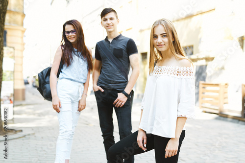 three happy friends students perfectly spend time together on a walk on the street. Friends posing together and looking at the camera, focus on the blondie girl