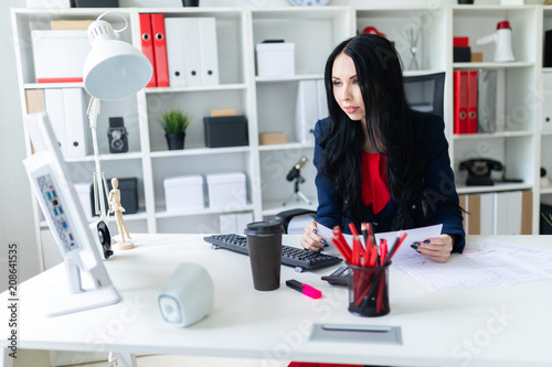 Beautiful young girl fills the documents, sitting in the office at the table.