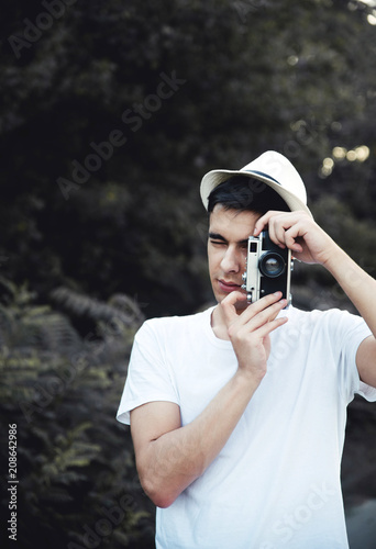 Young man with retro camera taking photos in nature