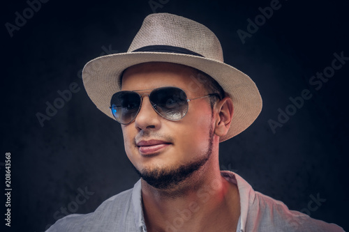 Close-up portrait of a handsome fashionable bearded man in a white shirt, panama hat and sunglasses.