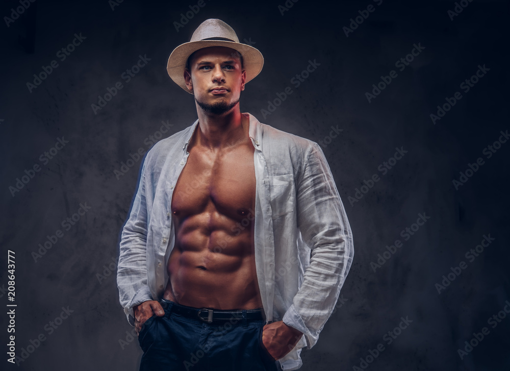 Portrait of a sexy handsome guy with muscular body in an unbuttoned white shirt and panama hat. 