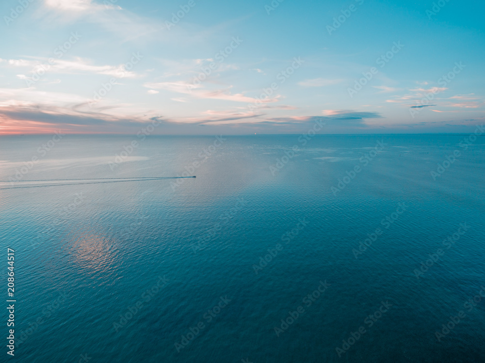 Tiny fishing boat sailing across calm sea at dusk