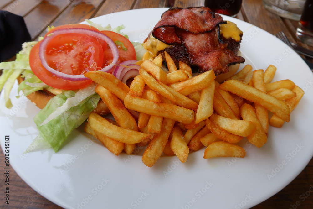 A plate of cheese burger with bacon, tomatos, onions and french fries A plate of cheese burger with bacon, tomatos, onions and french fries