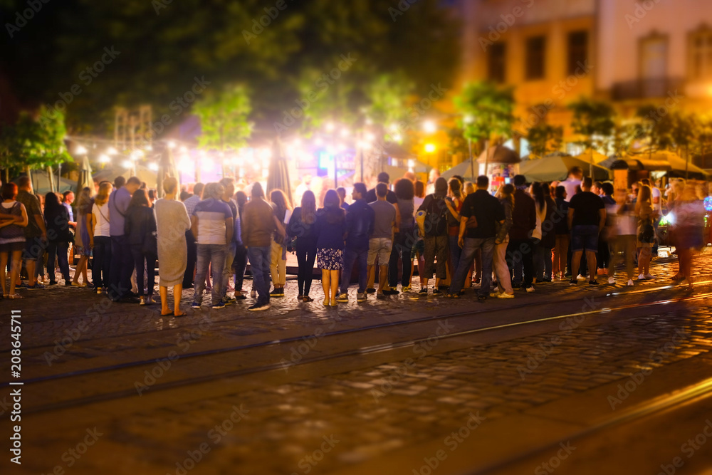 A crowd of people moving on the old european city night street defocused blurred abstract image