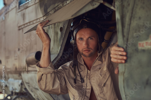 Portrait of a mechanic in uniform and flying near, standing under an old bomber airplane in the open air museum.