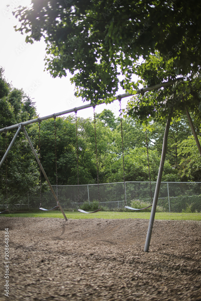 Empty Swing Set on Elementary School Playground Surrounded by Lush Spring Foliage