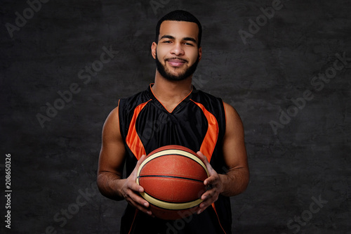 Smiling African-American basketball player in sportswear isolated over dark background.
