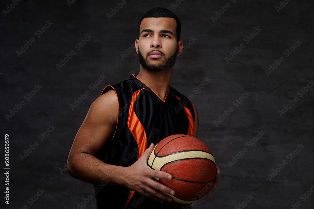 Young African-American basketball player in sportswear isolated over dark background.
