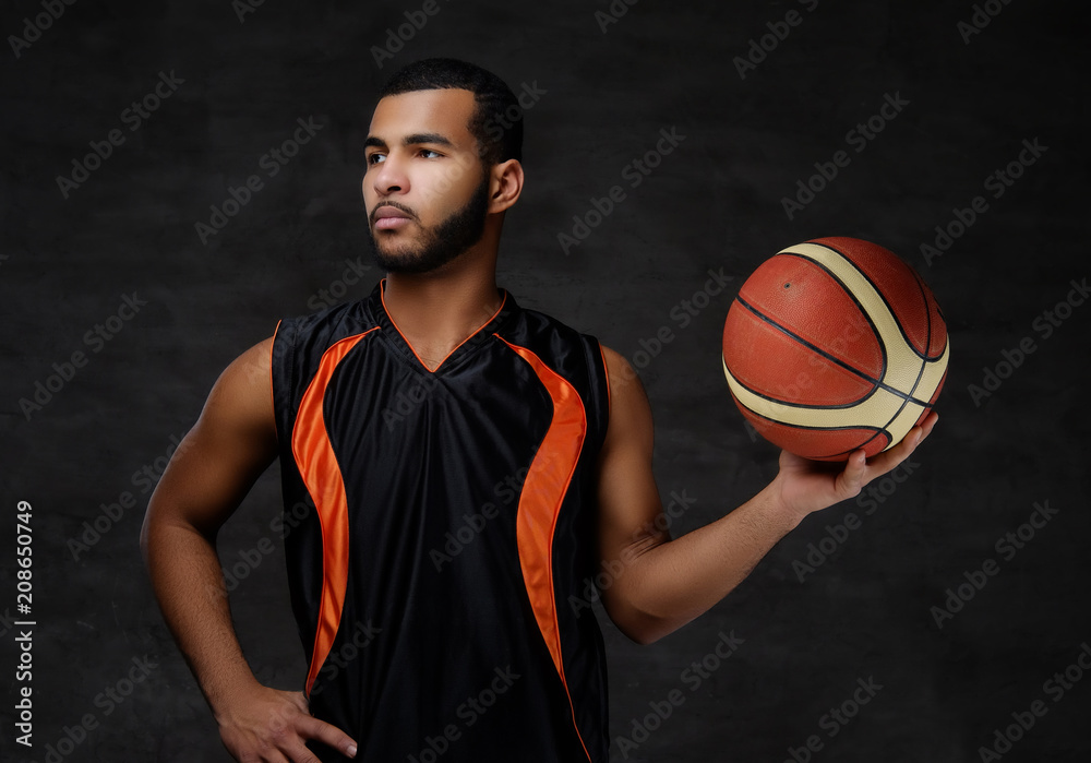 Young African-American basketball player in sportswear isolated over dark background.