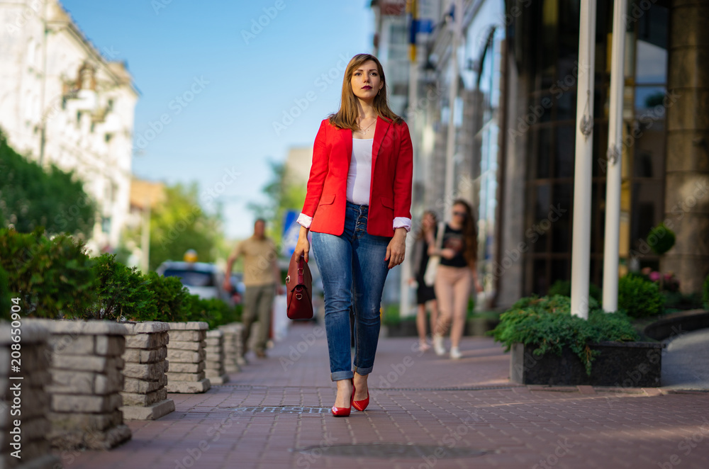 a girl in a red jacket and a lady's bag is walking along the street