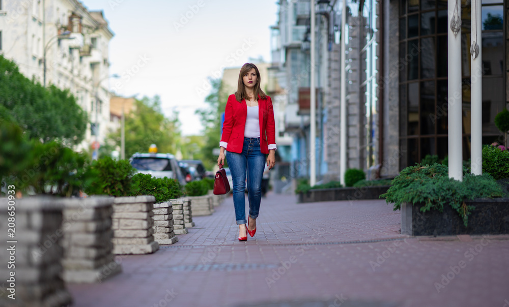 a girl in a red jacket and a lady's bag is walking along the street