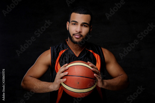 Young African-American basketball player in sportswear isolated over dark background.