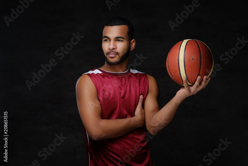 Young African-American basketball player in sportswear isolated over dark background.