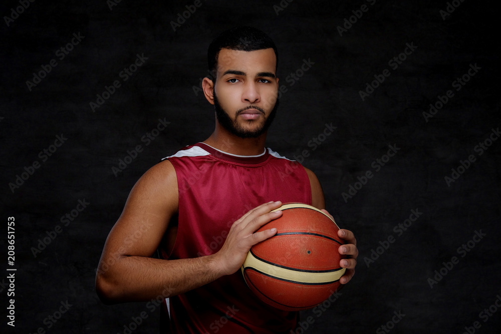 Young African-American basketball player in sportswear isolated over dark background.