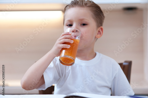 Close-up of charming little boy drinking freshly squeezed orange juice from glass goblet. Concept of healthy eating