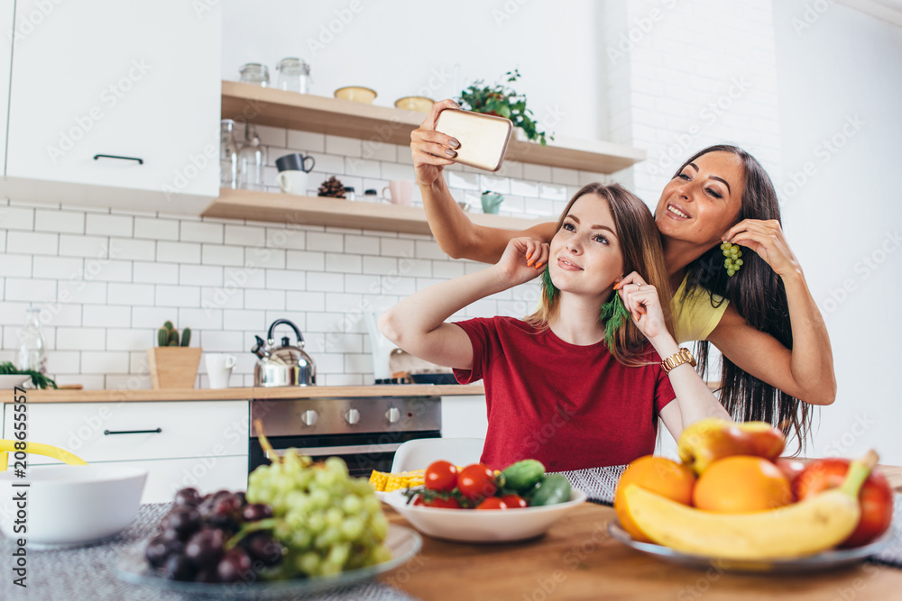 Women eating playing with vegetables in kitchen having fun and taking selfie