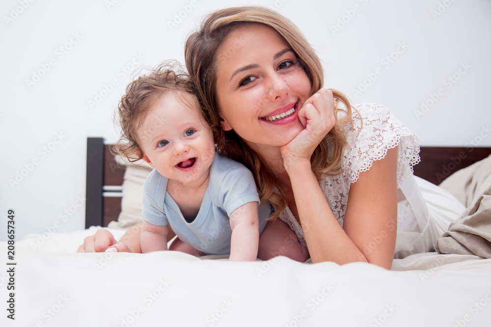 Young mother with her 7 month old little son dressed in pajamas are relaxing and playing in the bed at the weekend together, lazy morning, warm and cozy scene. Young mother with her 7 month old little son dressed in pajamas are relaxing and playing in the bed at the weekend together, lazy morning, warm and cozy scene.